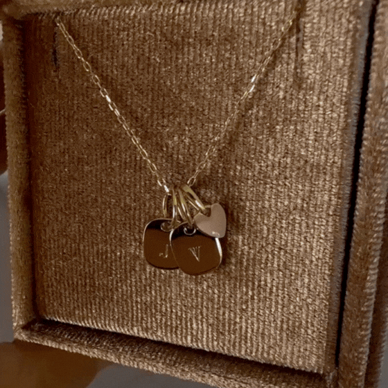 Bluebird Co's solid gold rectangular initial pendants stacked with a solid gold pink heart pendant on a solid gold necklace chain.