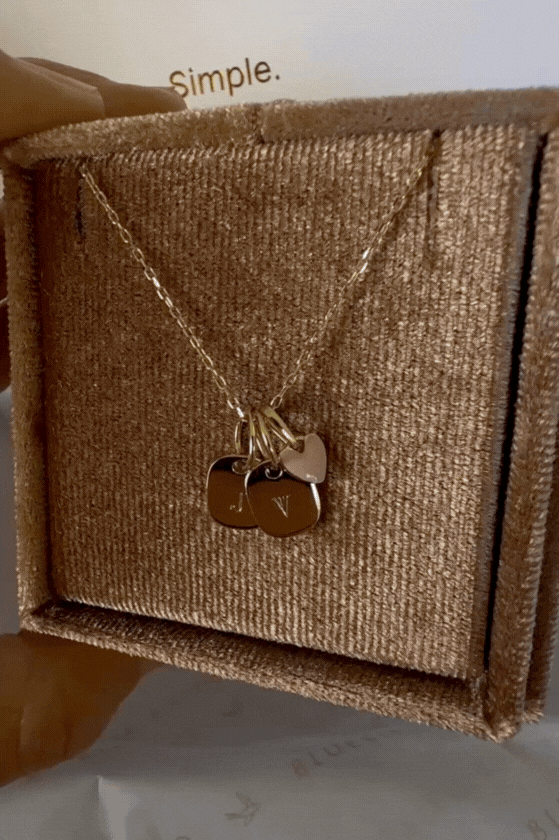 Bluebird Co's solid gold rectangular initial pendants stacked with a solid gold pink heart pendant on a solid gold necklace chain.