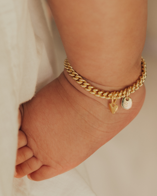 A baby wearing a delicate gold Cuban Link Chain Anklet with a heart charm and personalised pendant, designed as a timeless keepsake piece
