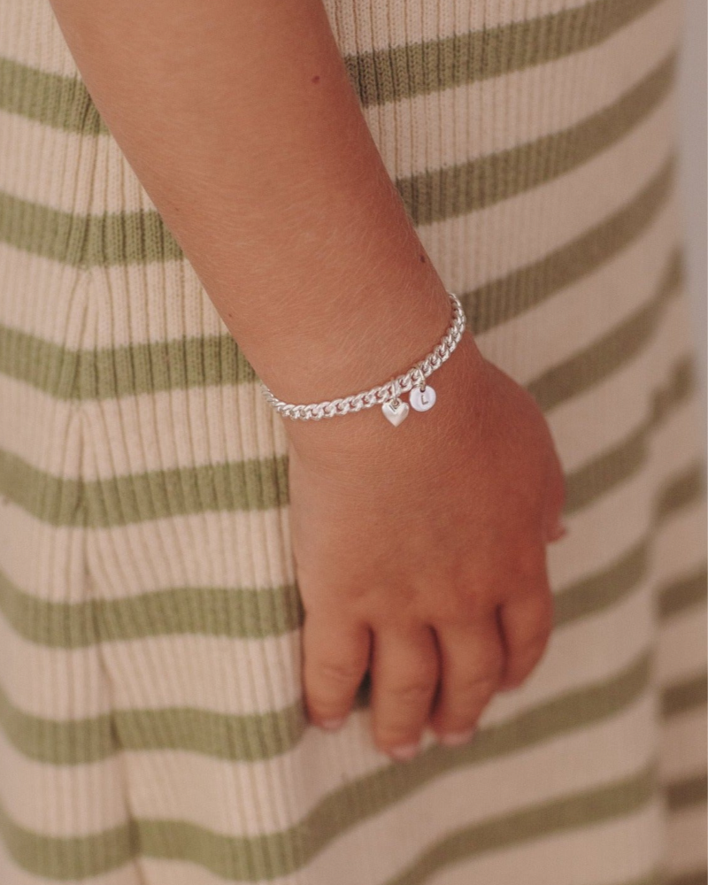 A young child wearing a Sweetheart Cuban Link Chain Bracelet featuring a polished heart charm and personalised initial pendant, crafted as a meaningful fine jewellery piece by Bluebird Co