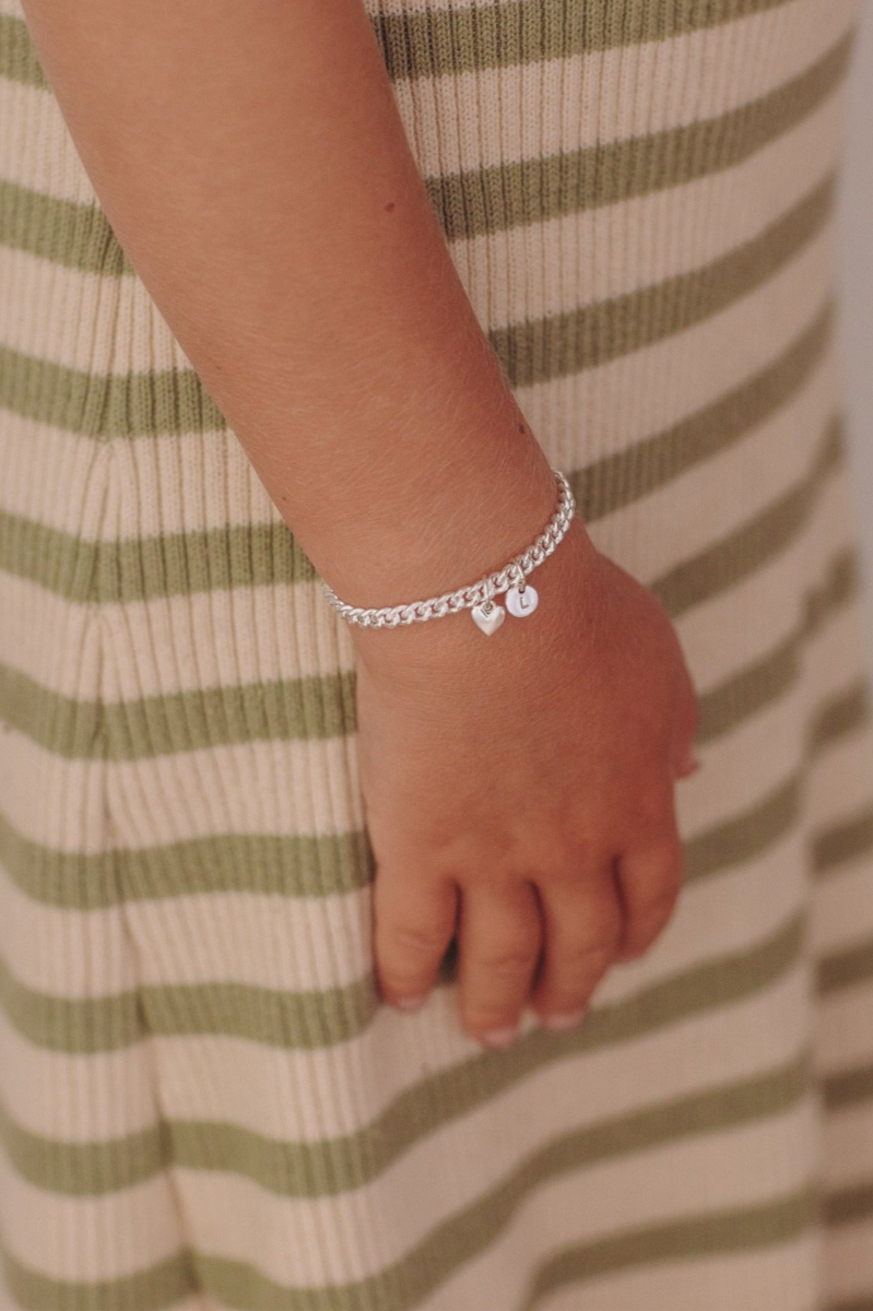 A young child wearing a Sweetheart Cuban Link Chain Bracelet featuring a polished heart charm and personalised initial pendant, crafted as a meaningful fine jewellery piece by Bluebird Co