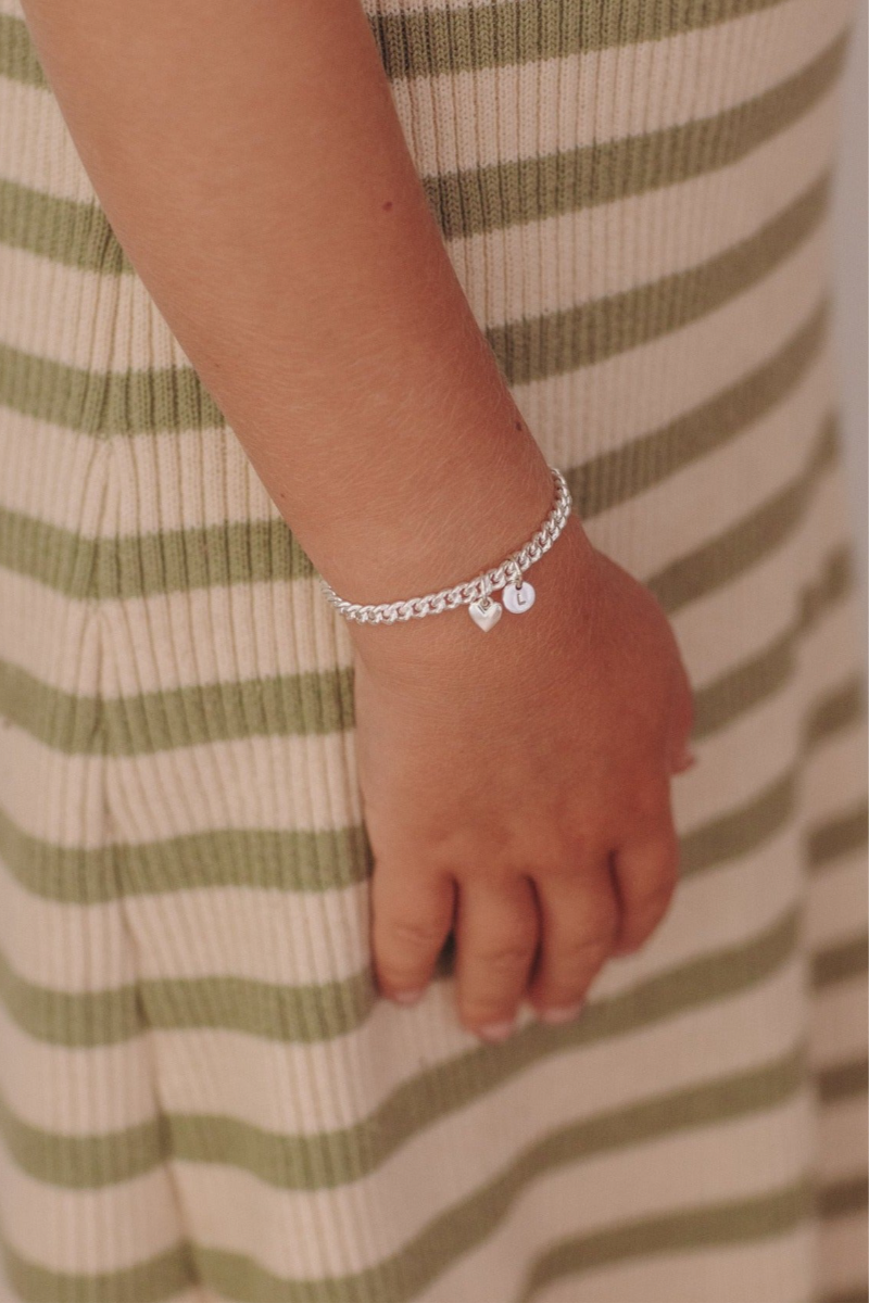 A young child wearing a Sweetheart Cuban Link Chain Bracelet featuring a polished heart charm and personalised initial pendant, crafted as a meaningful fine jewellery piece.
