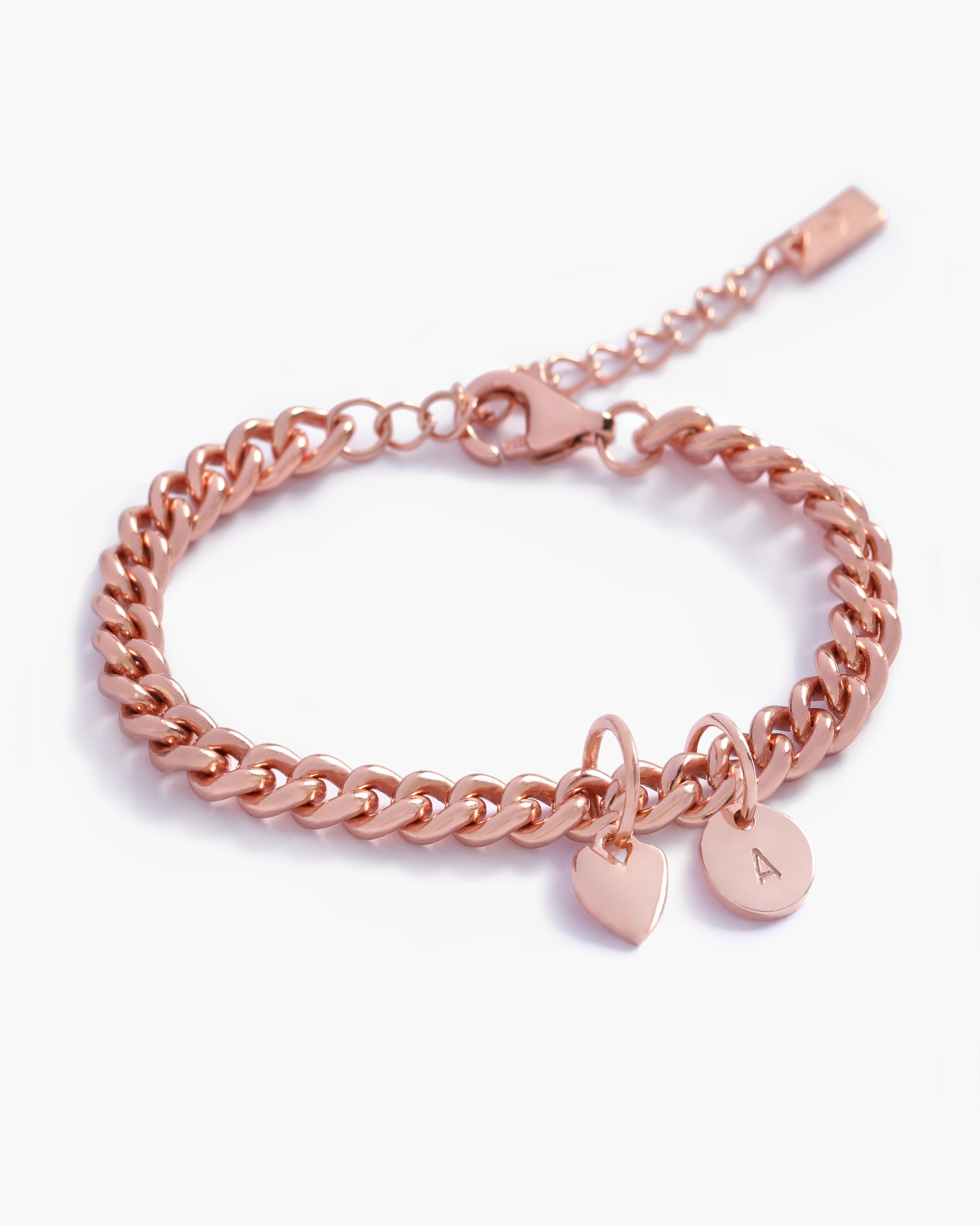 A rose gold Sweetheart Cuban Link Chain Bracelet adorned with a heart charm and engraved initial pendant, designed as a timeless personalised keepsake by Bluebird Jewellery