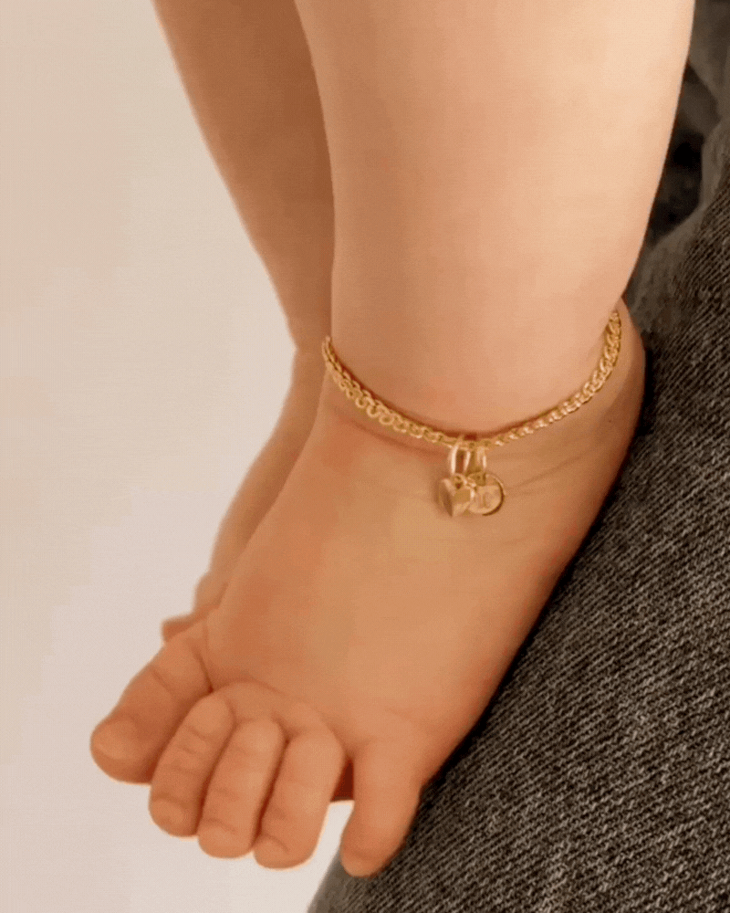 A baby is wearing a sweetheart lace chain anklet with an initial pendant on it.