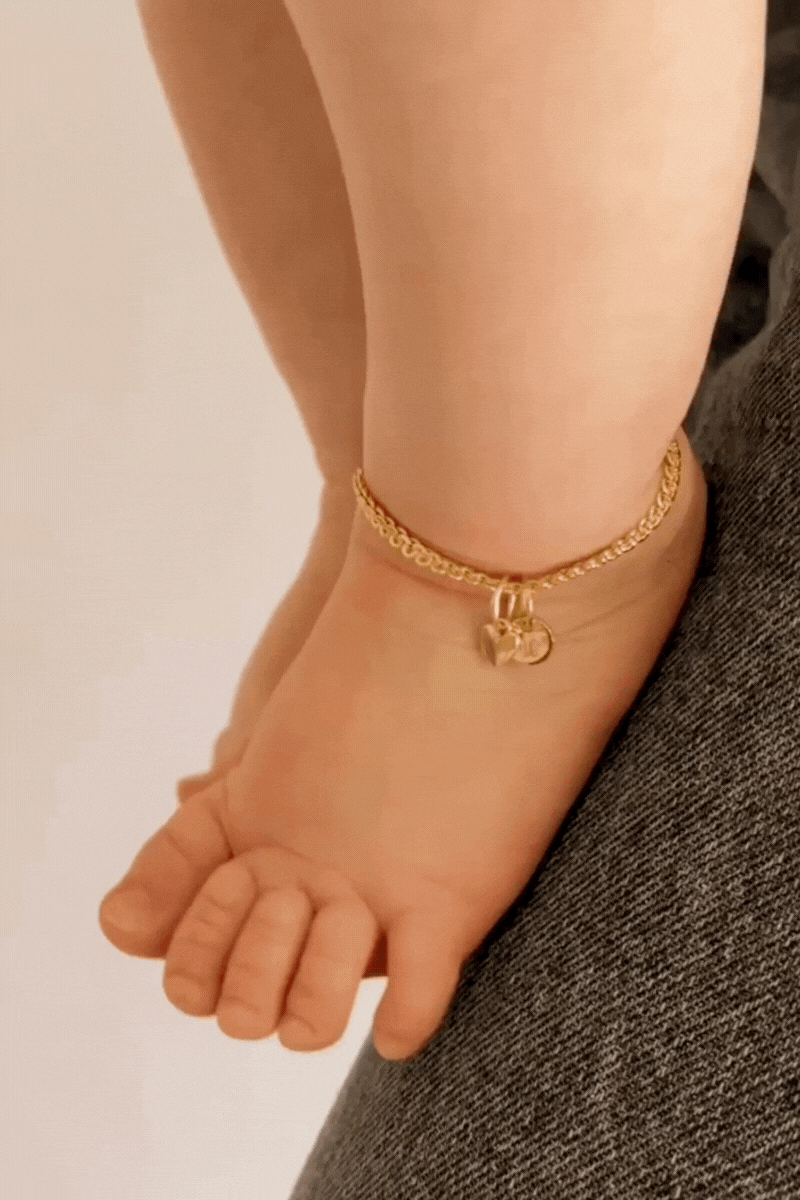 A baby is wearing a sweetheart lace chain anklet with an initial pendant on it.