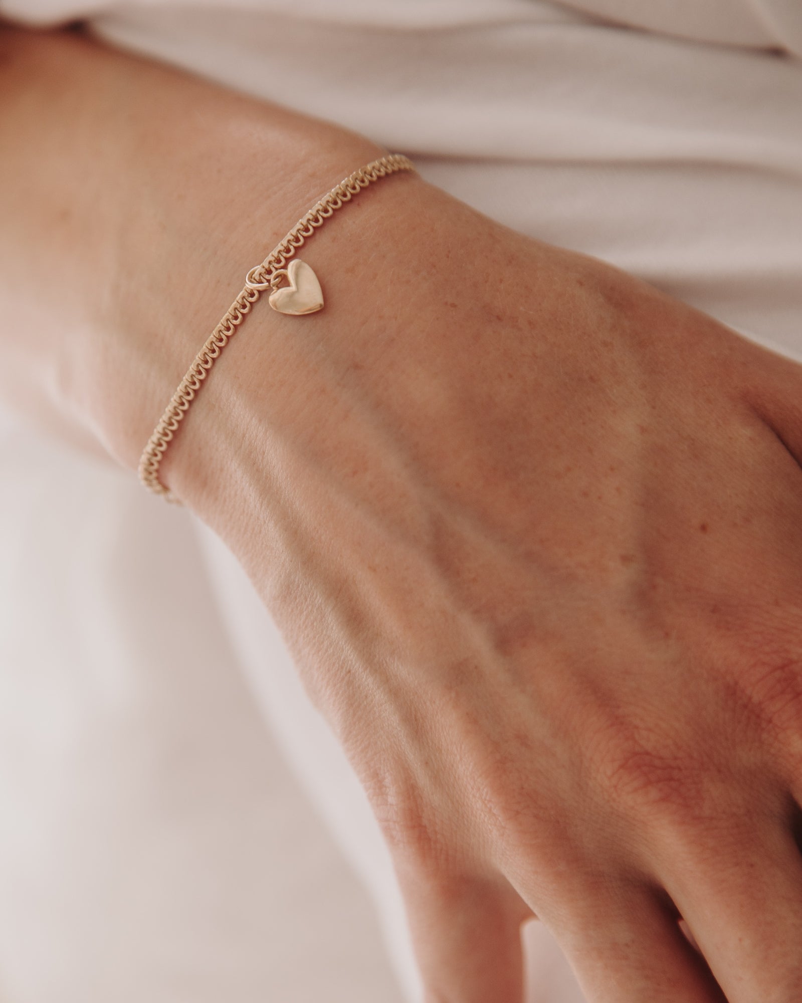 A close-up of a woman’s wrist adorned with the Sweetheart Lace Chain Bracelet and heart charm, designed as timeless minimalist jewellery by Bluebird Co
