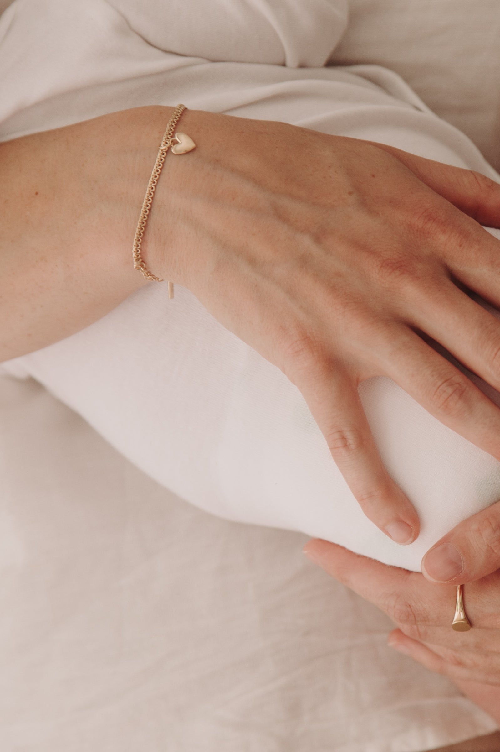 A close-up image capturing a woman holding a baby wearing a Lace Chain Bracelet with heart charm and matching gold signet ring, styled with refined simplicity.