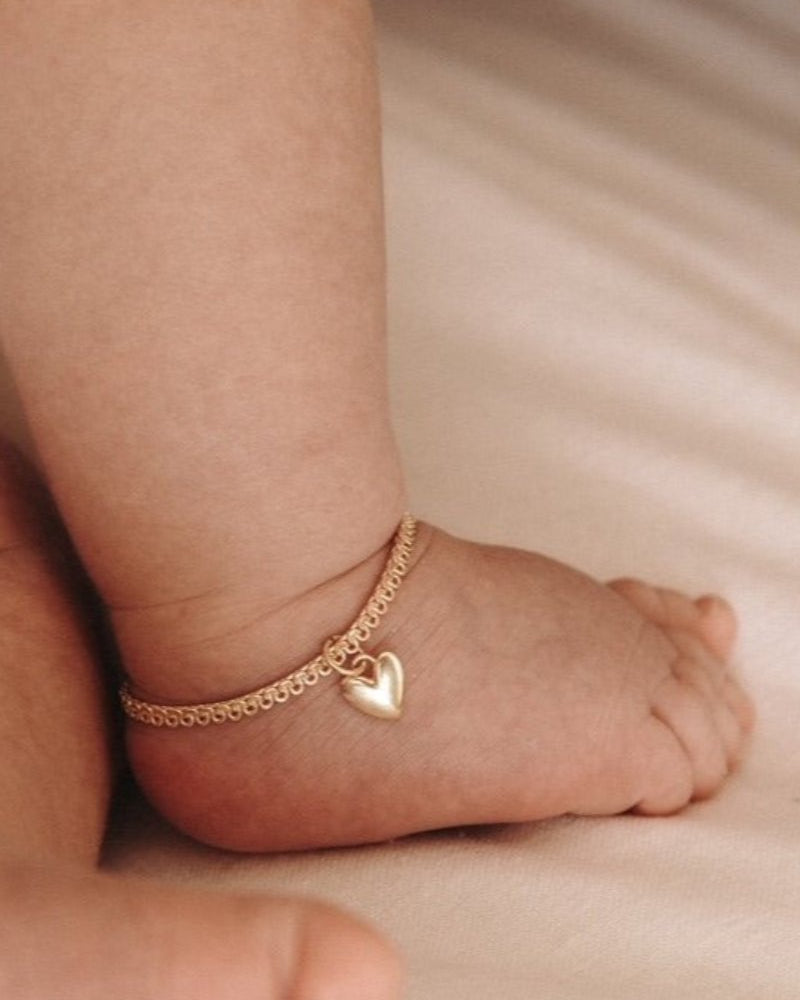 A baby is wearing a Sweetheart Lace Chain Anklet in Gold