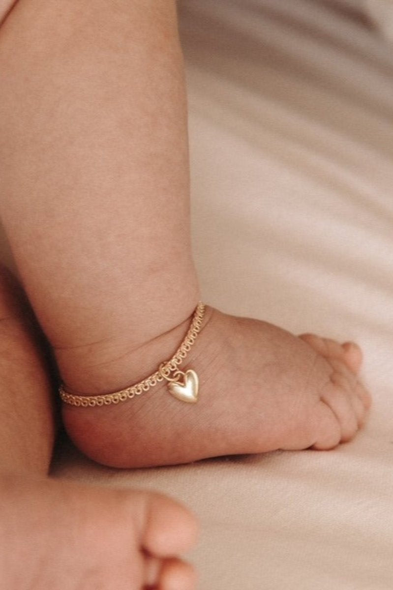 A baby is wearing a Sweetheart Lace Chain Anklet in Gold