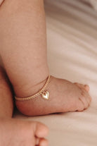 A baby is wearing a Sweetheart Lace Chain Anklet in Gold