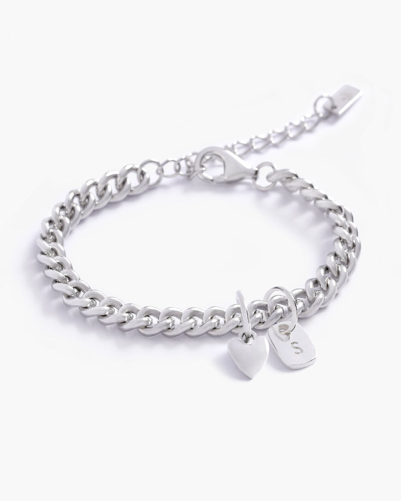 A detailed image of a silver Sweetheart Cuban Link Chain Bracelet with a heart charm and engraved initial pendant, designed as elegant personalised jewellery by Bluebird Co