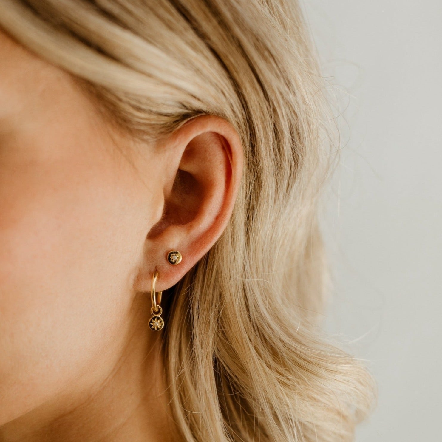 A Petite Vintage Pearl Stud sits next to a Petite Vintage Pearl Earring on a woman's earlobe.  The round surface with the seed pearl and vintage shaped star matches the charm on the hoop earring.