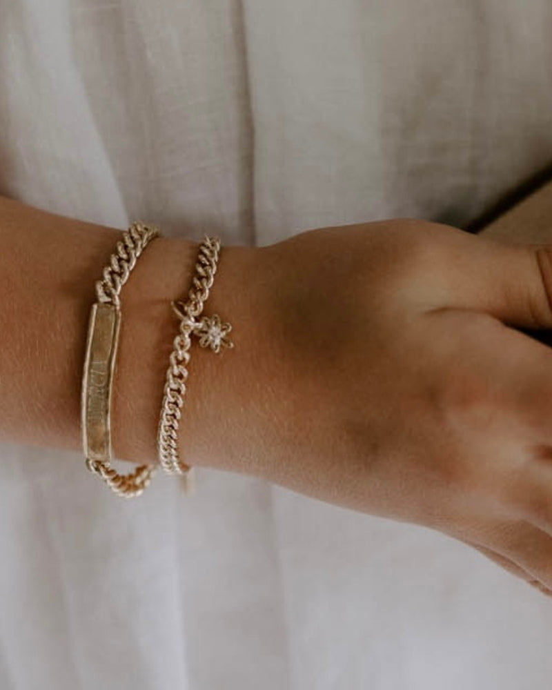 A Signature Bracelet is worn alongside a cuban link bracelet with a daisy pendant on it