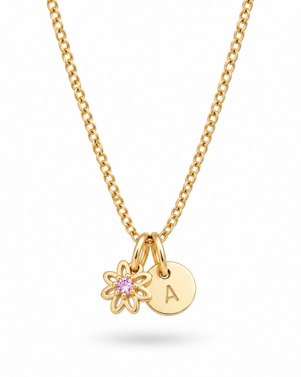 A gold chain necklace featuring a small gold flower charm with a pink gemstone and a round gold initial 'A' disc charm, shown on a clean white background.