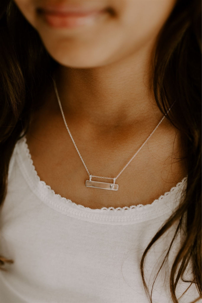 Close up of Darling Bar Necklace in silver with engraved heart worn on child’s chest