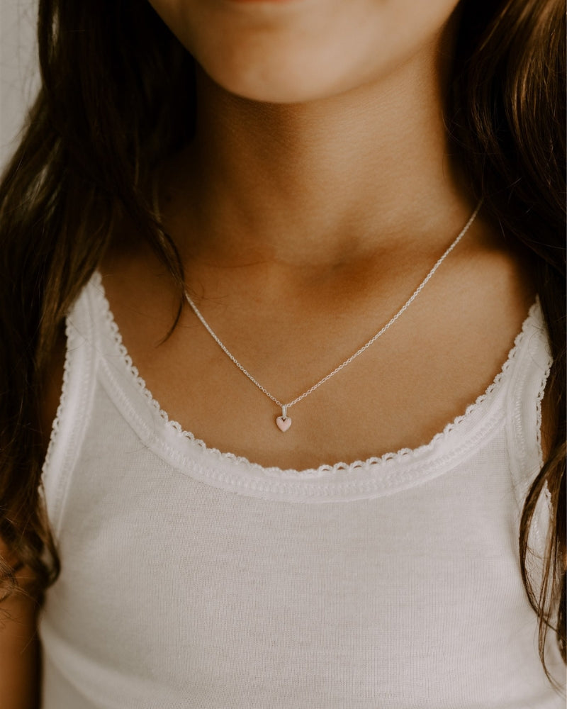 The Pink Petite Darling necklace with its soft pink heart pendant on a fine cable chain is worn by a young girl.