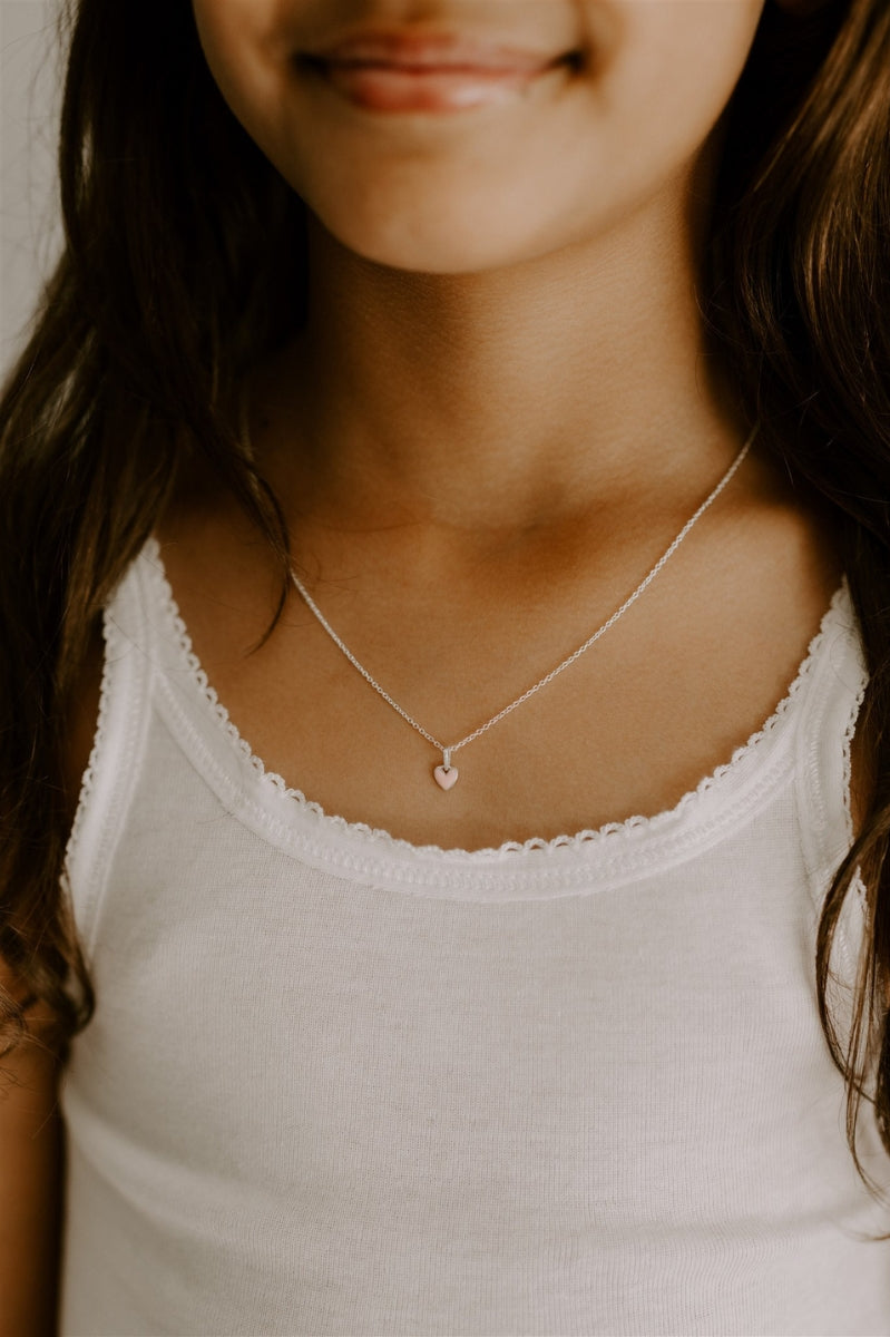 The Pink Petite Darling necklace with its soft pink heart pendant on a fine cable chain is worn by a young girl.
