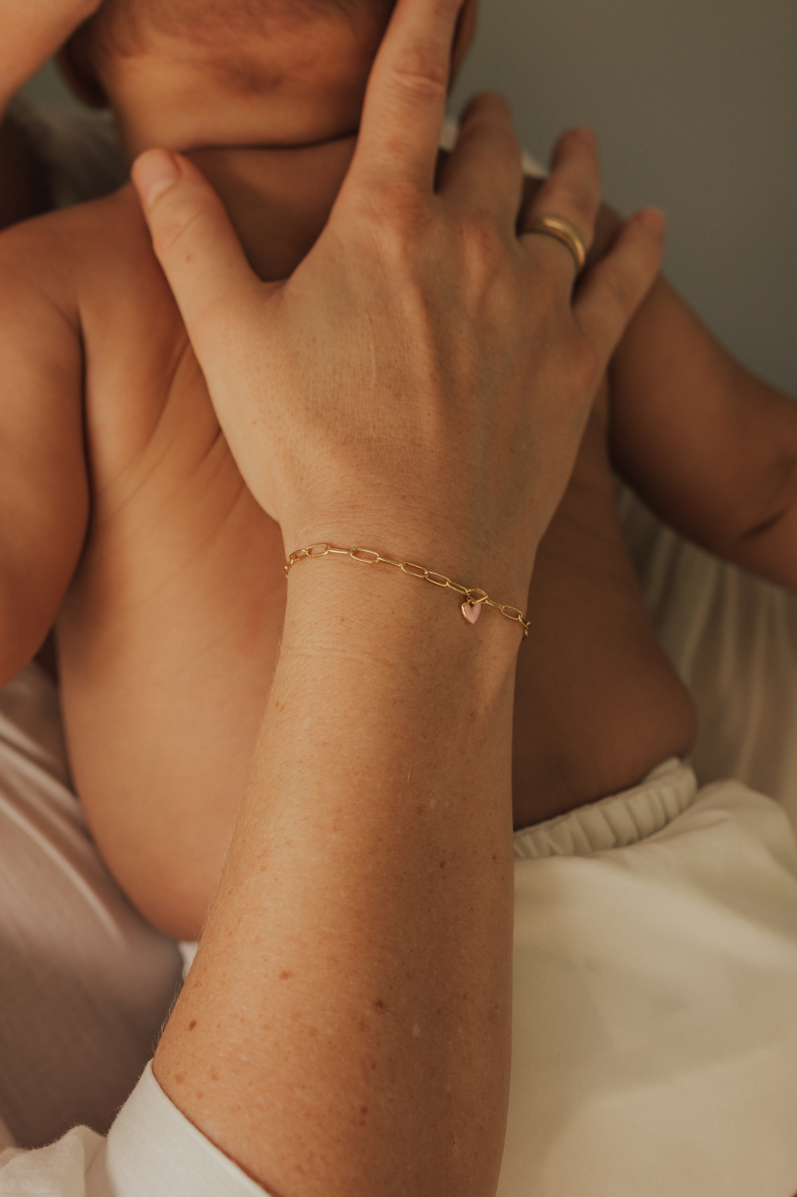 Adult wearing Darling Posie Bracelet Gold with pink heart charm while cuddling baby, a timeless jewellery keepsake