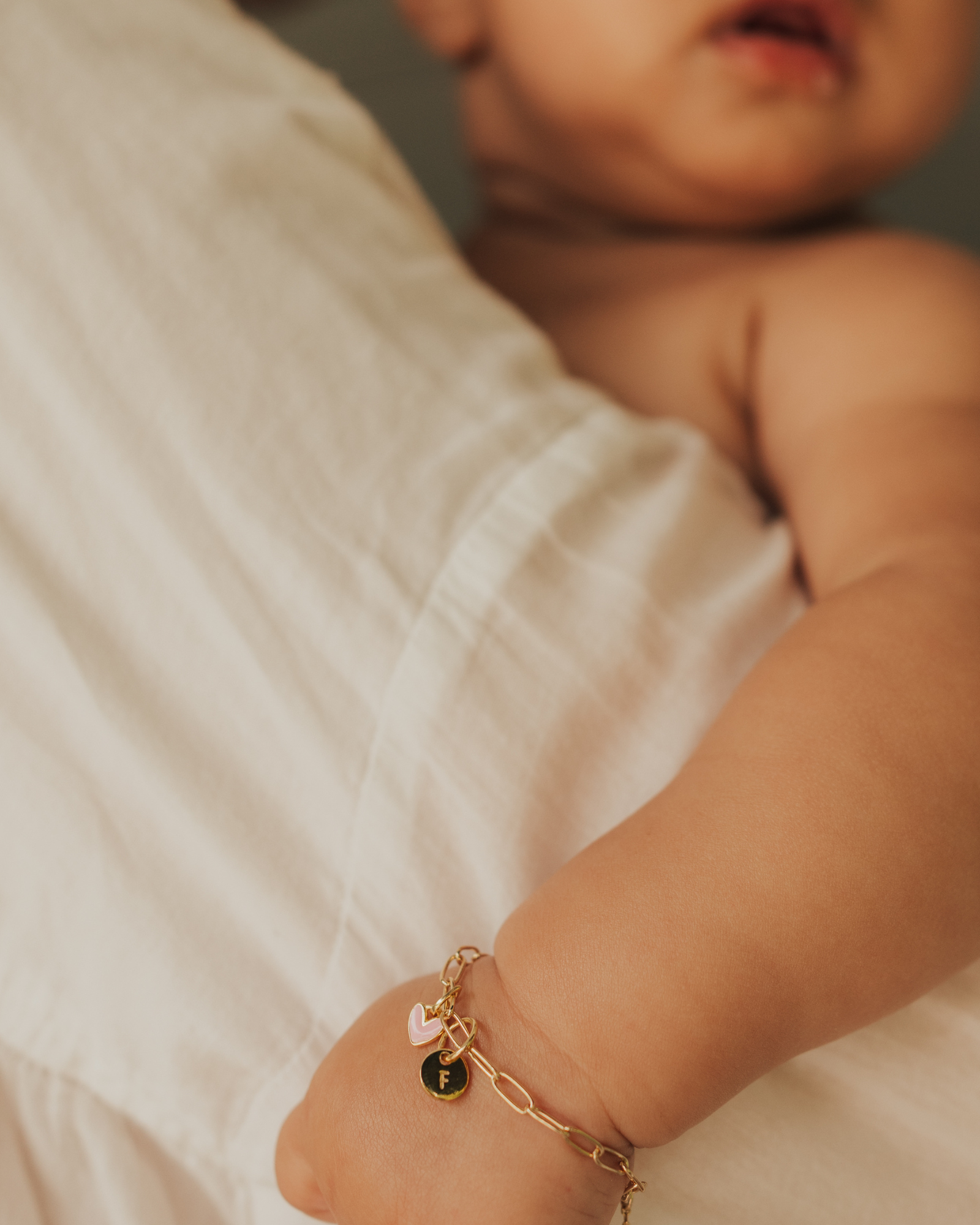Darling Posie Bracelet Gold worn by baby, featuring pink heart and engraved charm for a personalised keepsake look by Bluebird Jewellery.