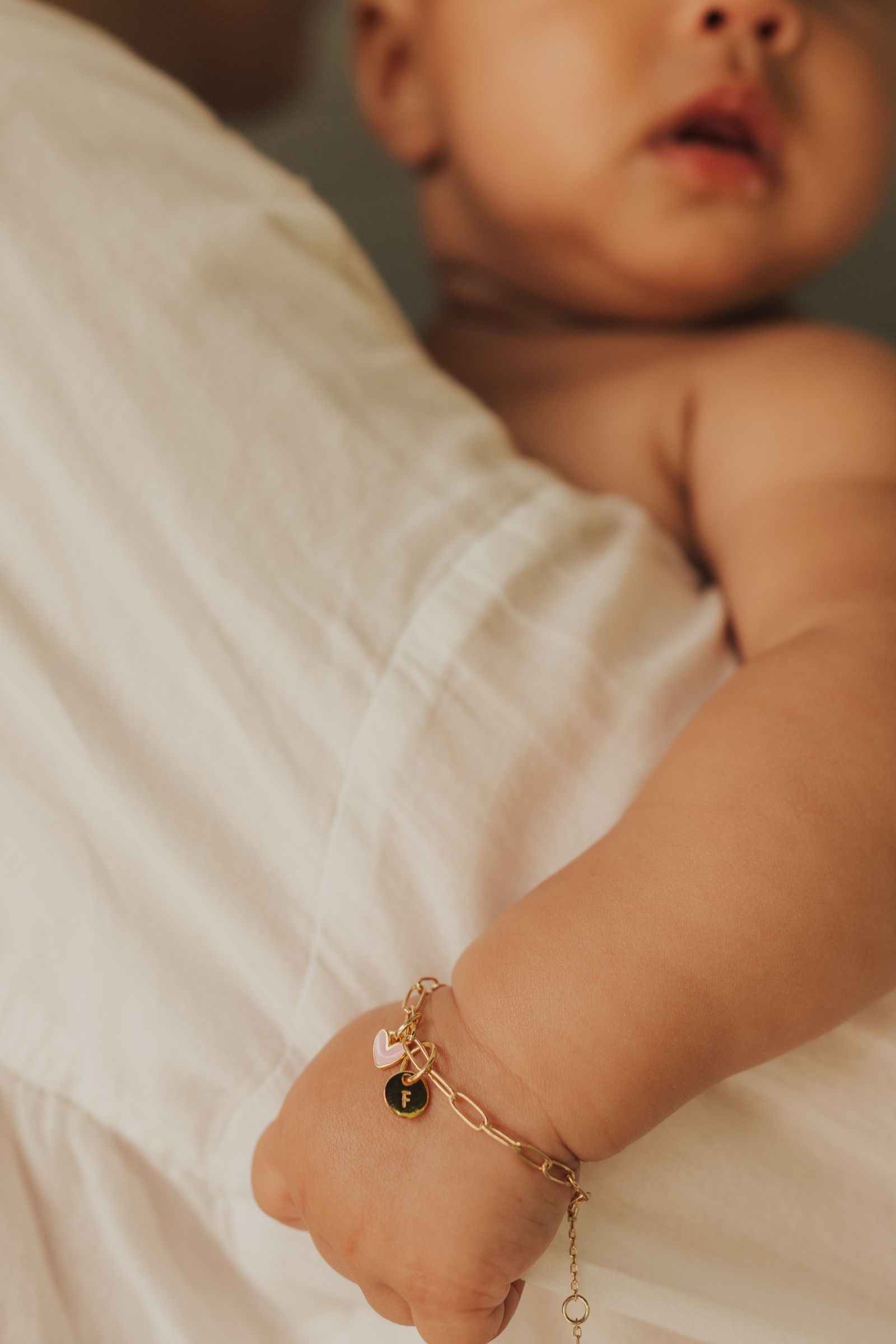 Darling Posie Bracelet Gold worn by baby, featuring pink heart and engraved charm for a personalised keepsake look by Bluebird Jewellery.