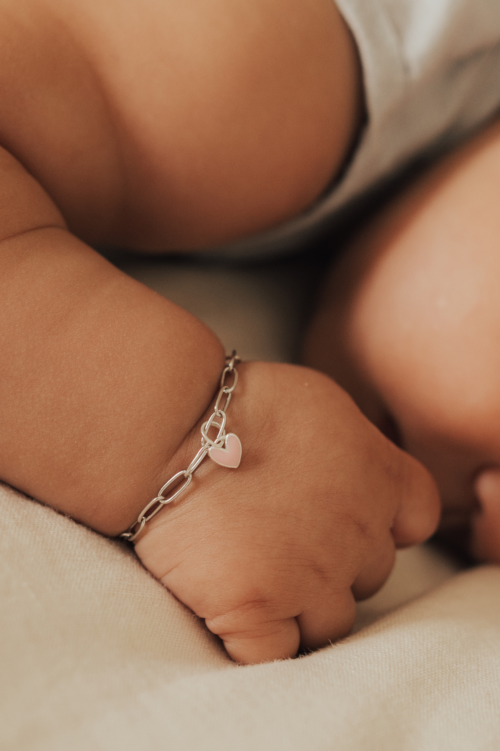 A delicate close-up of a newborn wearing a sterling silver Darling Posie Bracelet featuring a pink heart charm, designed as a meaningful keepsake by Bluebird Jewellery.