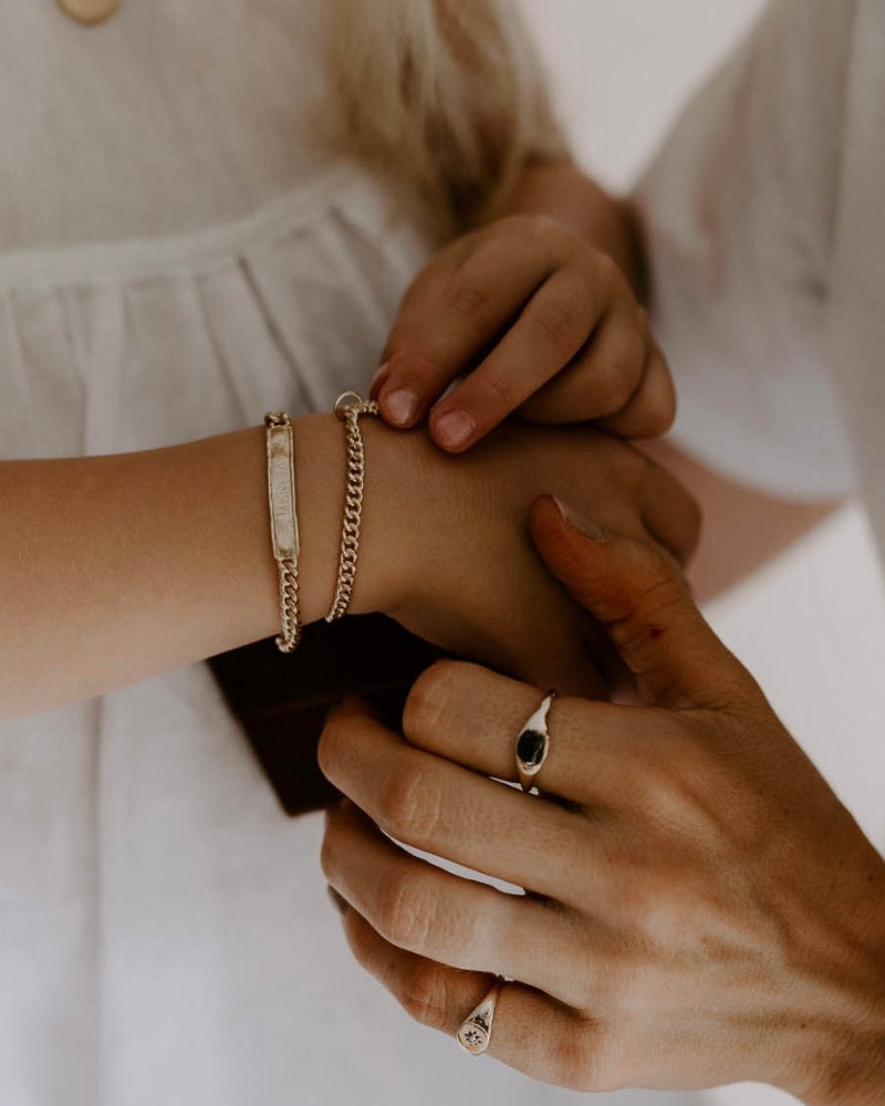 Child wearing engraved gold bracelet while adult helps fasten it, both with gold signet rings, meaningful keepsake jewellery by Bluebird Co