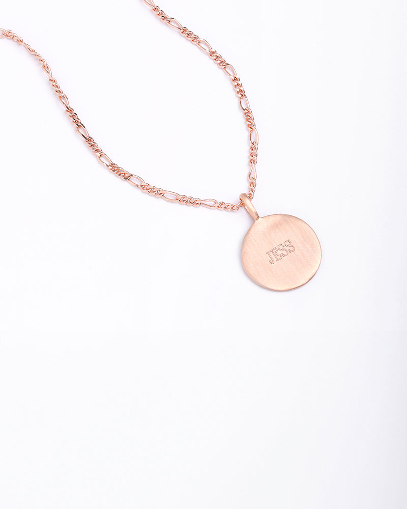 Rose gold disc necklace engraved with ‘JESS’, photographed flat with Figaro chain