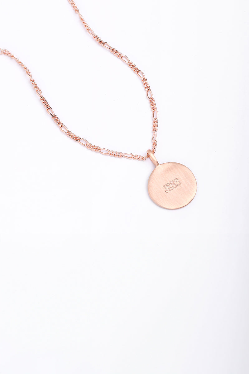 Rose gold disc necklace engraved with ‘JESS’, photographed flat with Figaro chain