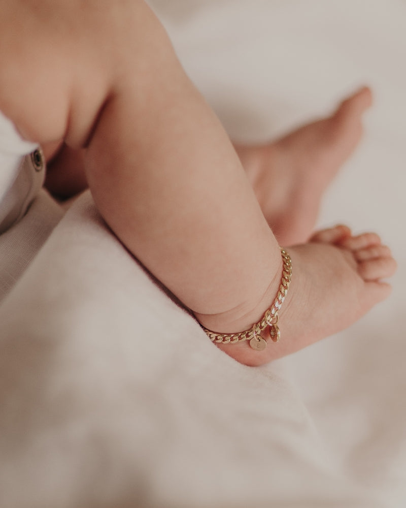 An image of a baby's ankle wearing a Cuban Link Chain with a vintage pearl pendant with personalised initial pendant, designed as a timeless keepsake.