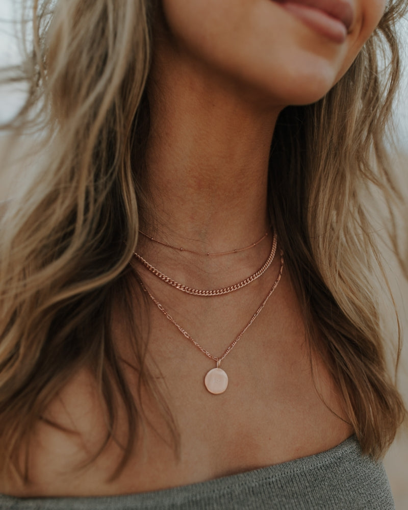 Woman wearing rose gold disc necklace layered with fine rose gold chains