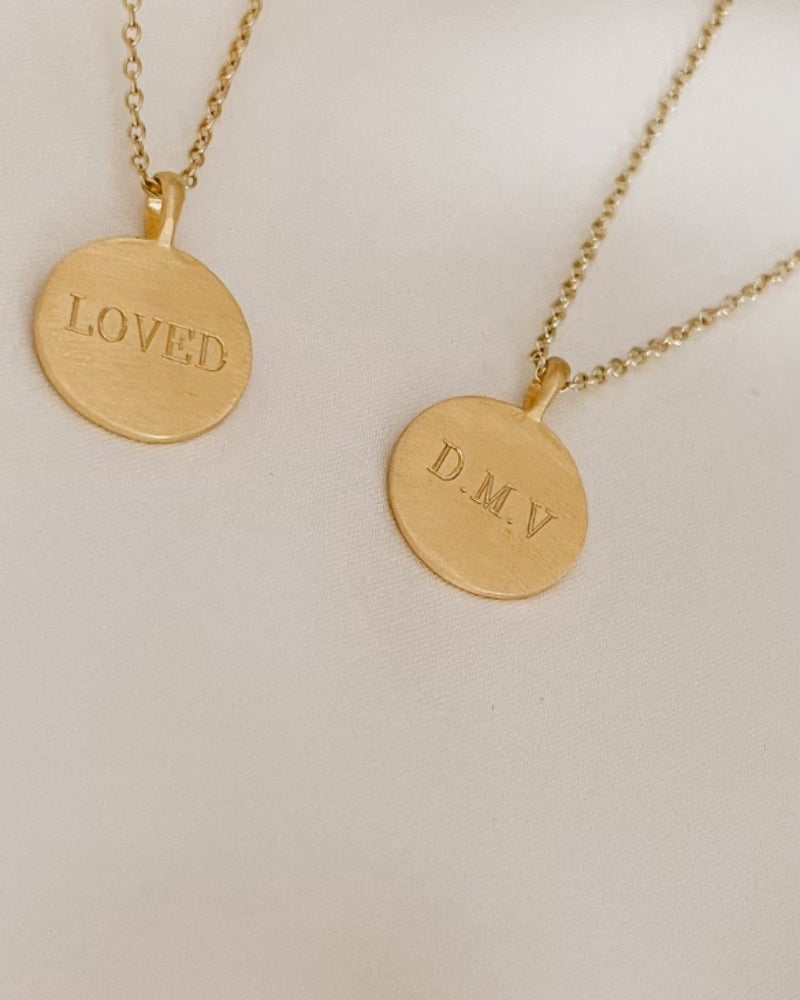 Two personalised gold pendant necklaces engraved with 'LOVED' and initials 'D.M.V'.