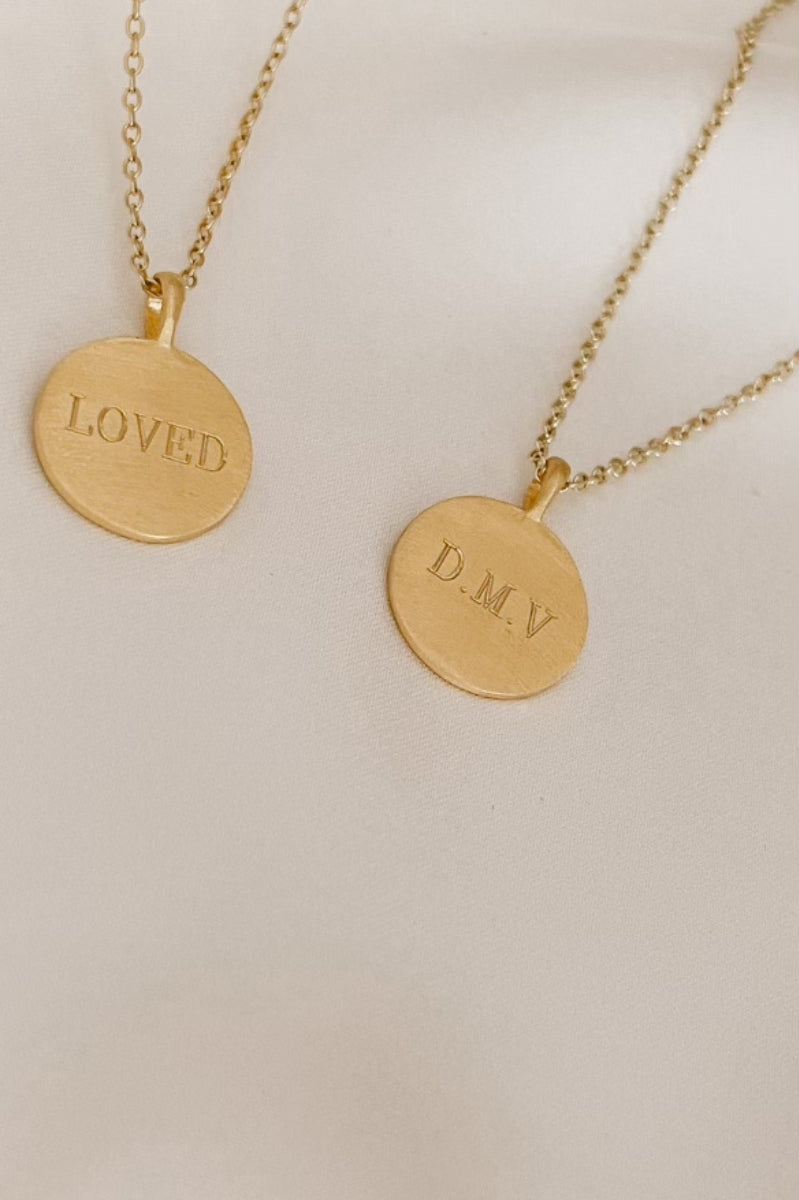 Two personalised gold pendant necklaces engraved with 'LOVED' and initials 'D.M.V'.