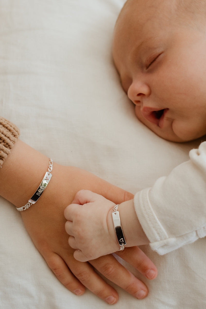 Baby and child holding hands, both wearing Pink Darling Silver Bracelets with engraved bars and pink heart pendant.