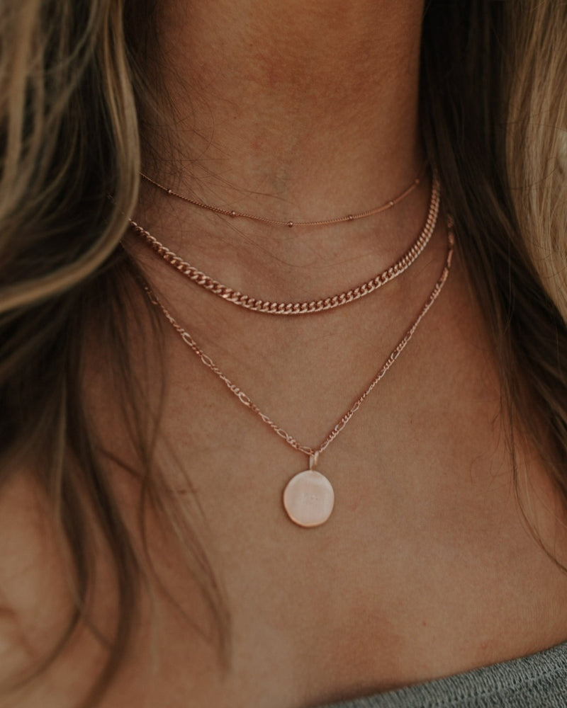 Close-up of engraved rose gold necklace worn with two other delicate gold chains