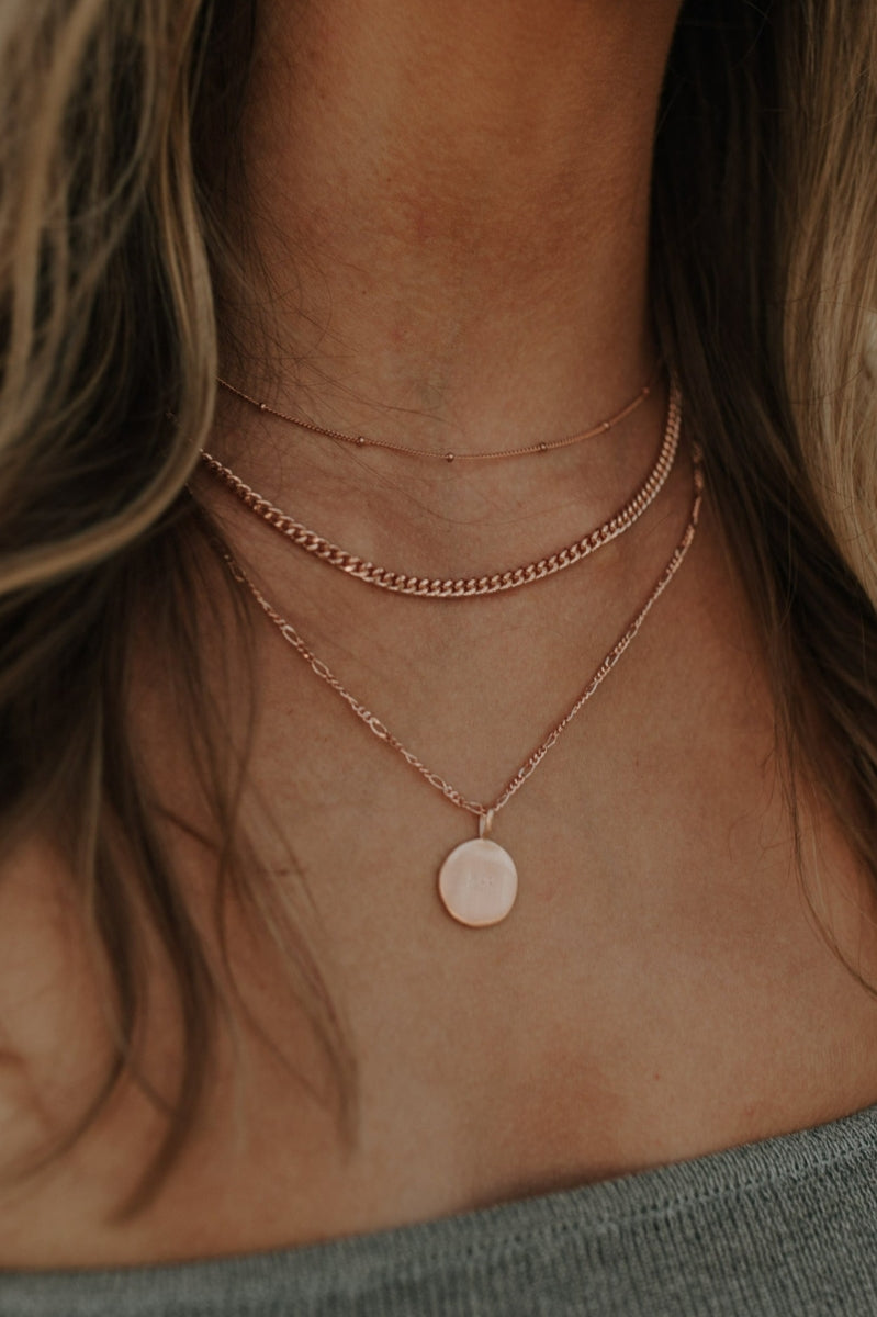 Close-up of engraved rose gold necklace worn with two other delicate gold chains