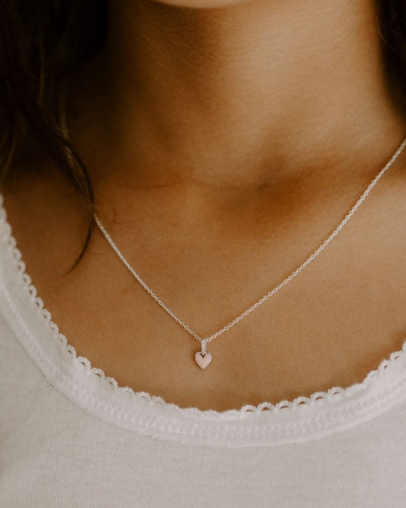 A young girl is wearing darling petite silver necklace with pink heart pendant