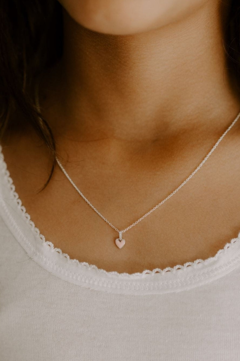 A young girl is wearing darling petite silver necklace with pink heart pendant