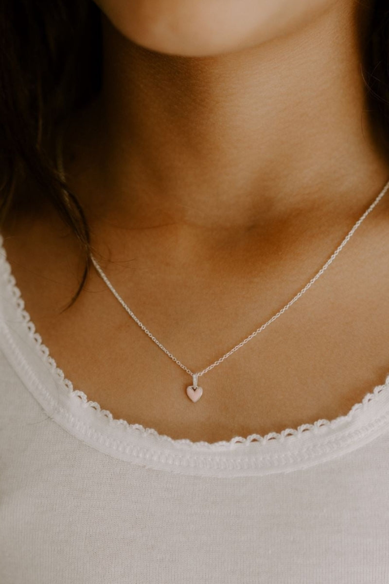A young girl is wearing darling petite silver necklace with pink heart pendant