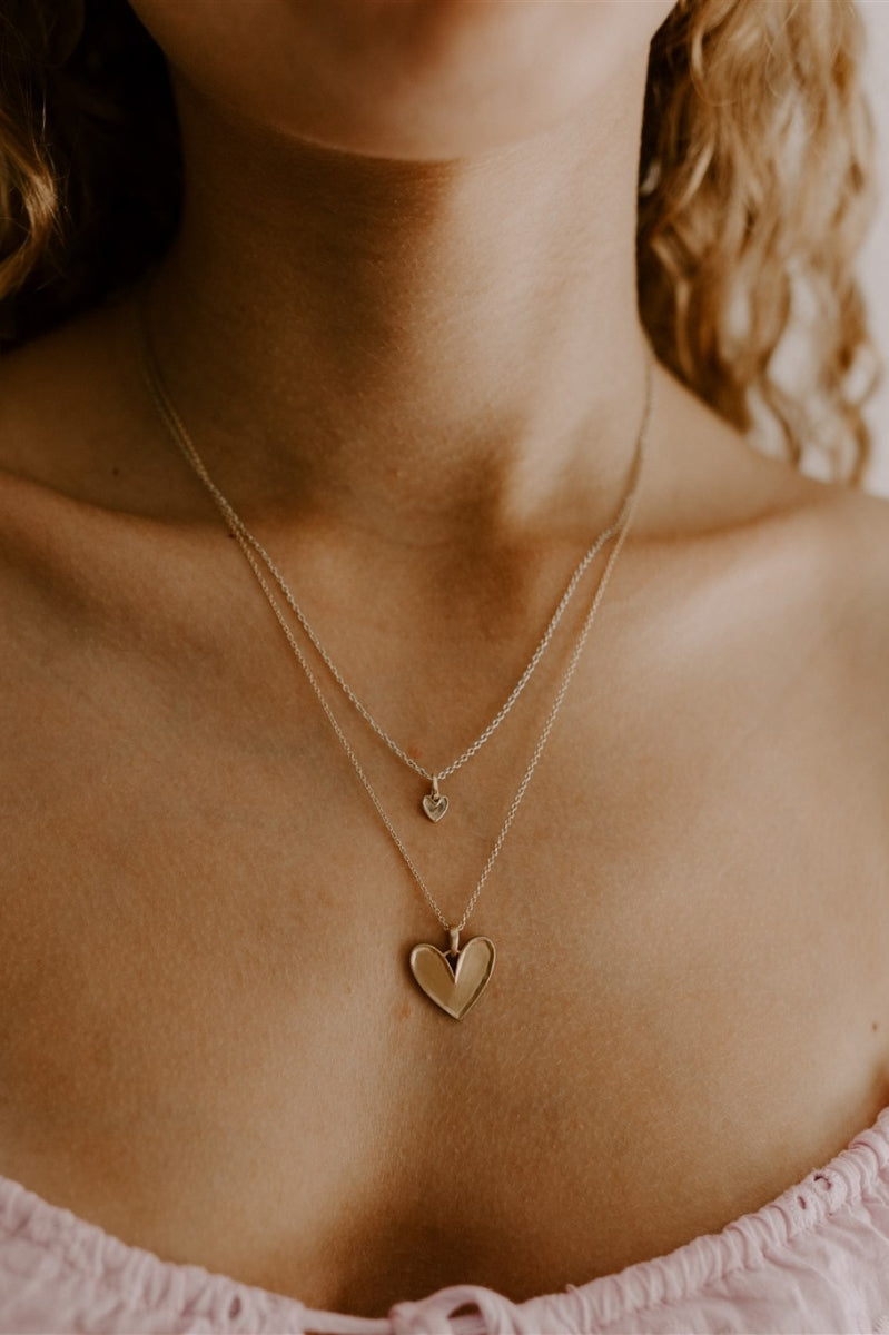 A teenage girl is wears the Petite Darling Necklace Gold layered with the Darling Necklace in Gold. The two necklaces compliment one another with a matte finish with finely raised edges and an organic surface.