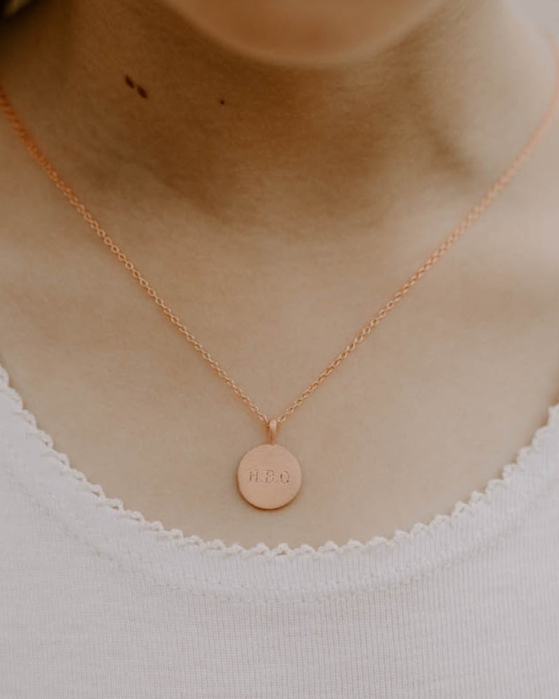 Petite Signature Necklace in rose gold shown worn with initials engraved on round pendant resting just below the collarbone.
