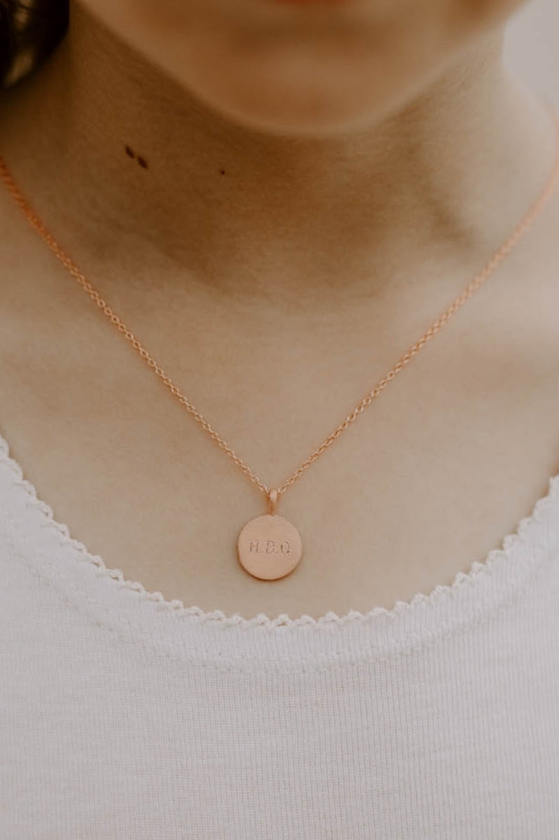 Petite Signature Necklace in rose gold shown worn with initials engraved on round pendant resting just below the collarbone.
