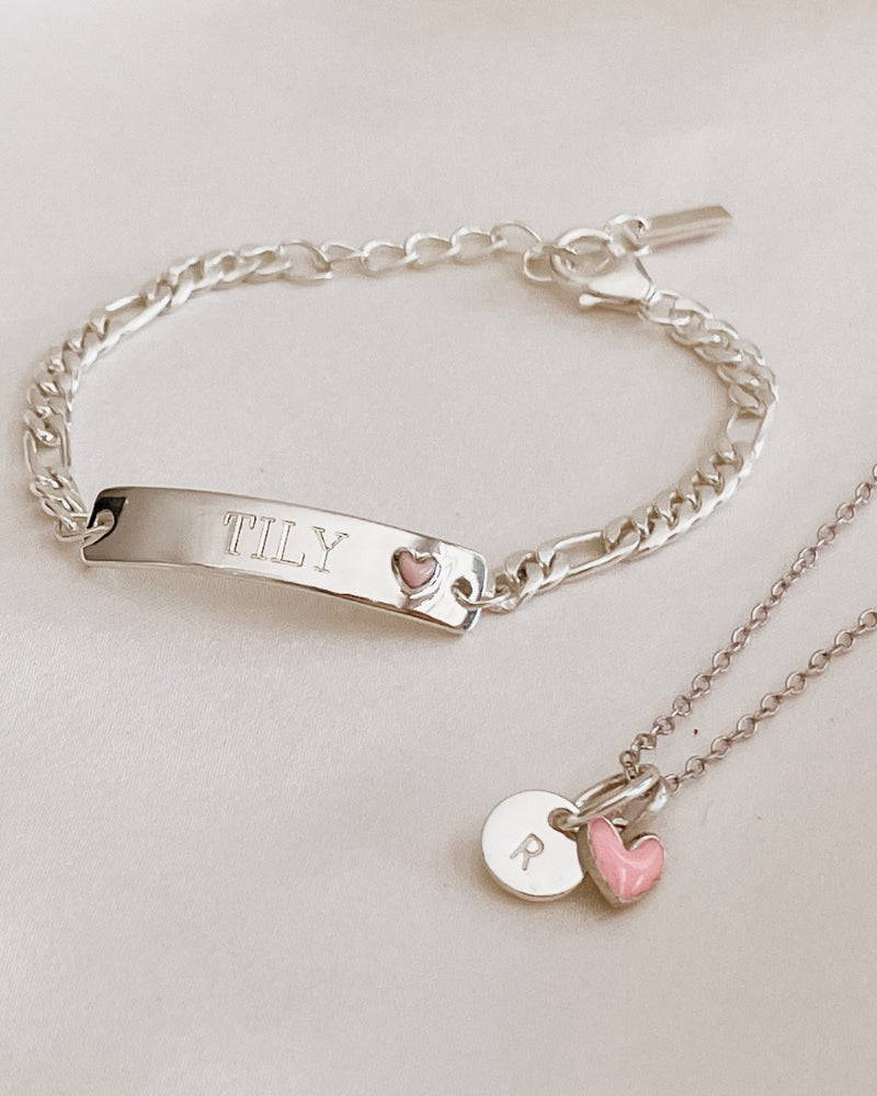 A Pink Darling Bracelet sits alongside a Pink Petite Darling Necklace with an engraved initial pendant and pink heart by Bluebird Jewellery.
