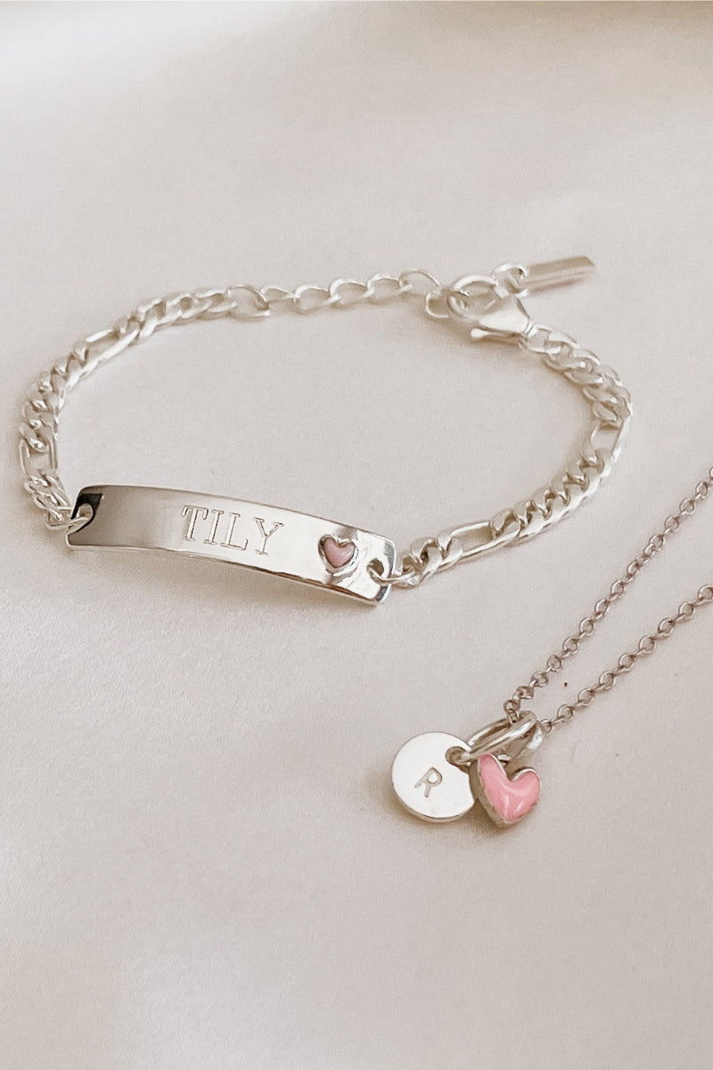 A Pink Darling Bracelet sits alongside a Pink Petite Darling Necklace with an engraved initial pendant and pink heart.