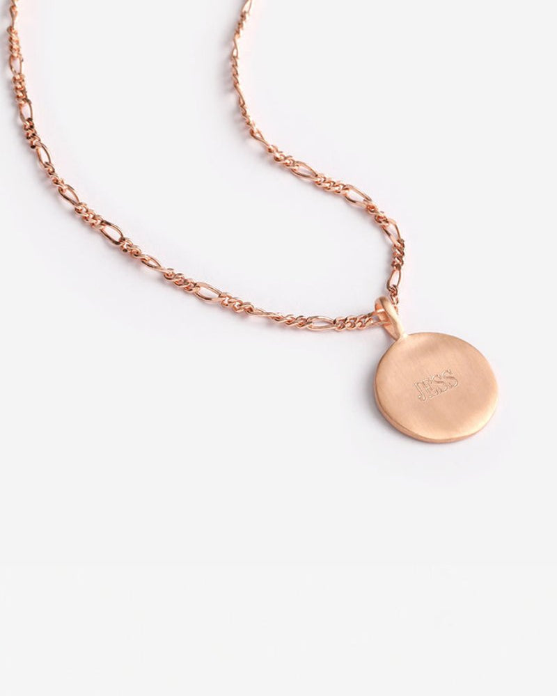 Engraved rose gold disc necklace on Figaro chain shown against plain background