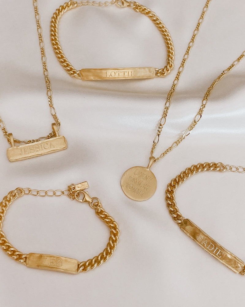 Flatlay showing gold signature bar necklace with matching bracelets and pendant. Personalised gift-ready jewellery.
