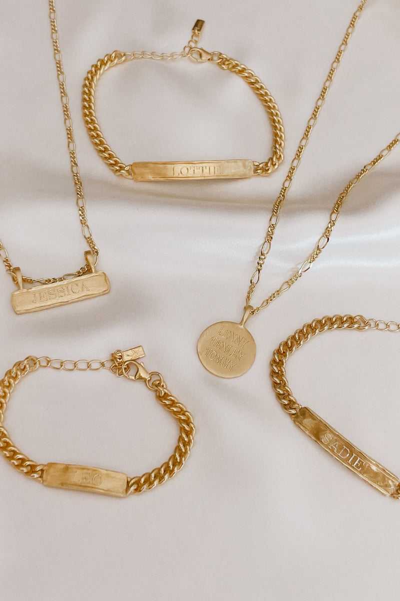 Flatlay showing gold signature bar necklace with matching bracelets and pendant. Personalised gift-ready jewellery.