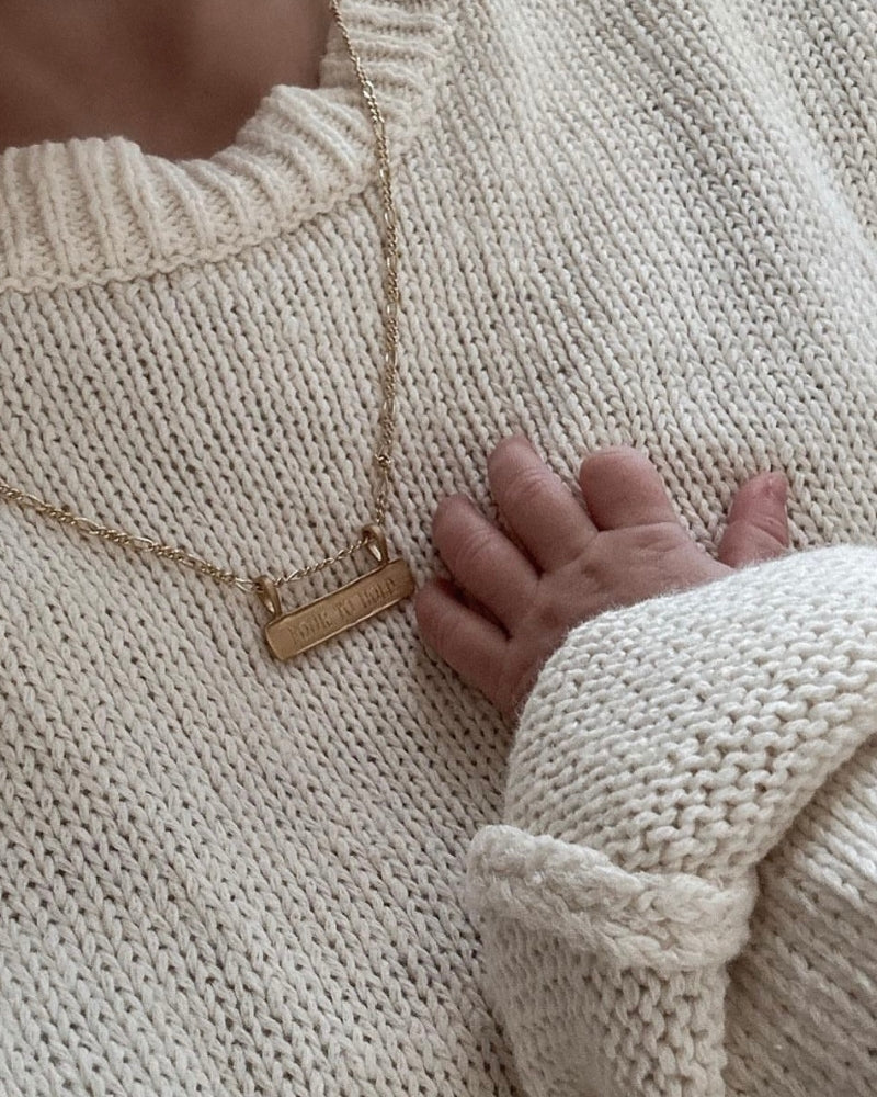 Personalised gold signature bar necklace engraved with names, shown beside a newborn’s hand. Ideal new mum gift.