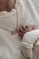 Personalised gold signature bar necklace engraved with names, shown beside a newborn’s hand. Ideal new mum gift.