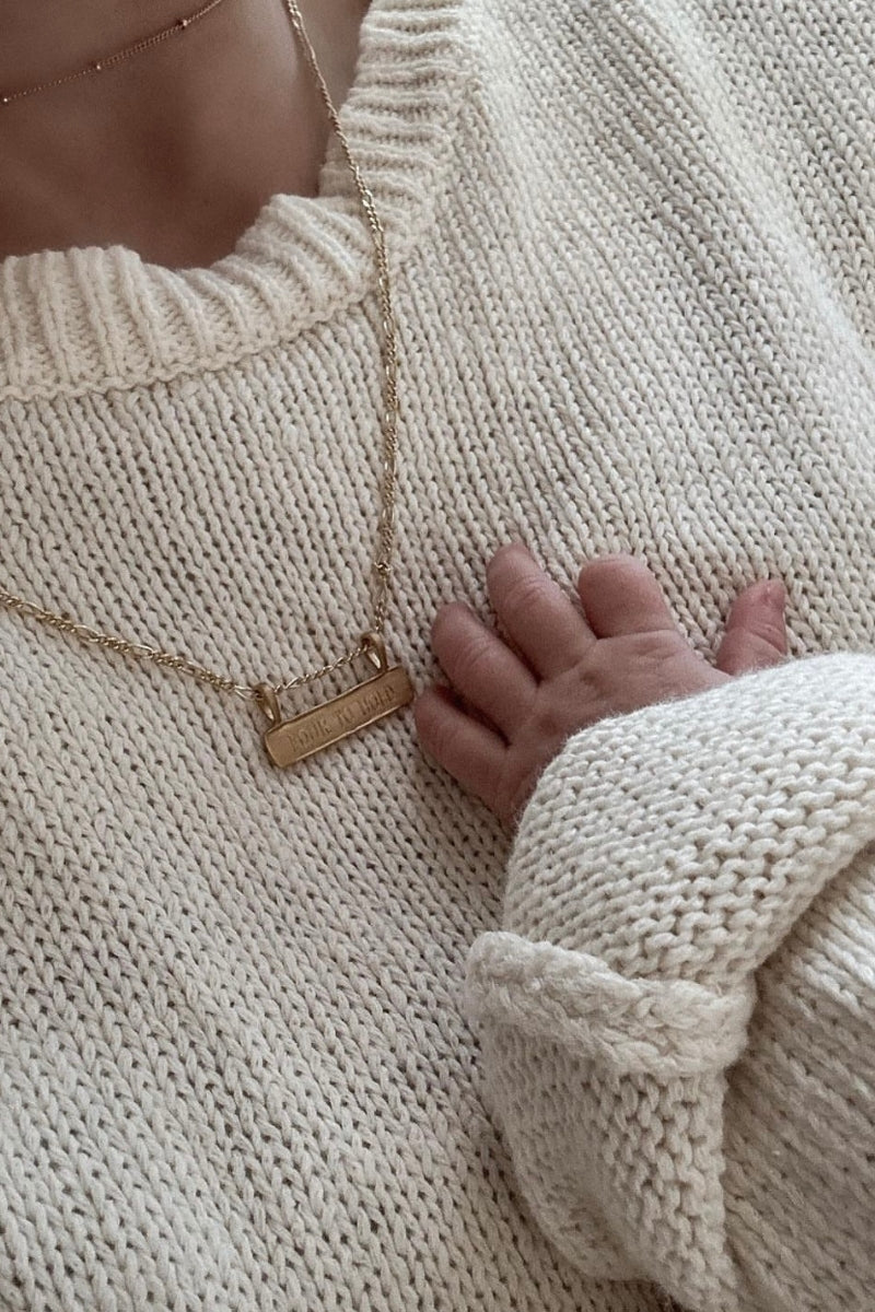 Personalised gold signature bar necklace engraved with names, shown beside a newborn’s hand. Ideal new mum gift.