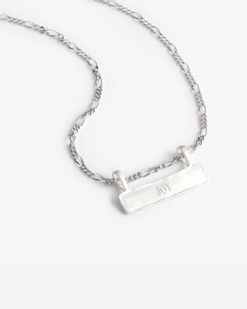 Engraved Signature Bar Necklace Silver featuring the word "JOY" on a figaro-style chain. A timeless, handcrafted sterling silver keepsake.